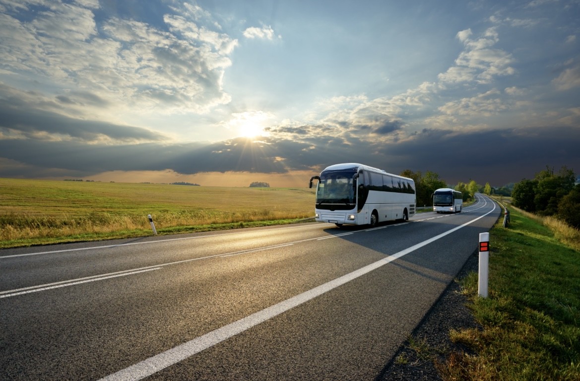 Bus driving down a flat road with the sun in the background