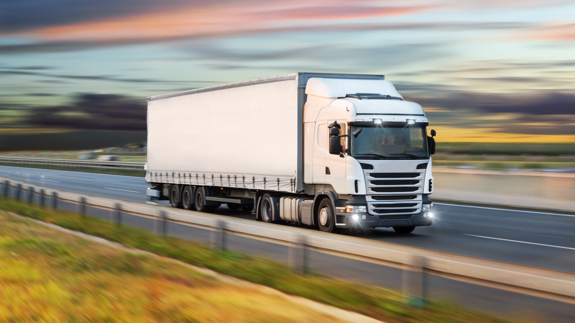 Commercial semi-truck transporting freight on a highway during sunset