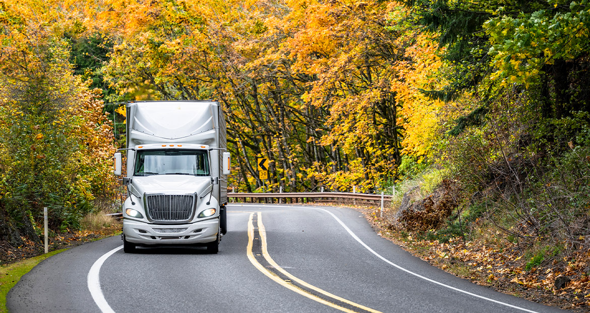 A semi truck driving a curved road with fall foliage in the background representing advanced diesel engine innovations