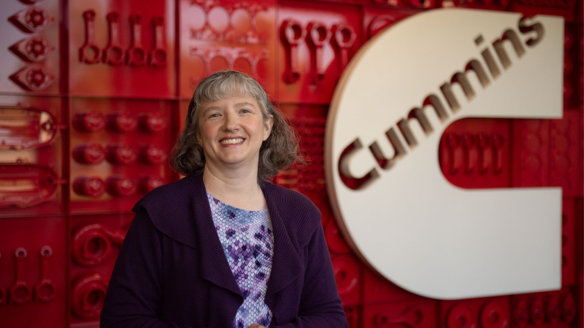 Jennifer, a Cummins engineer, stands in front of a Cummins logo display