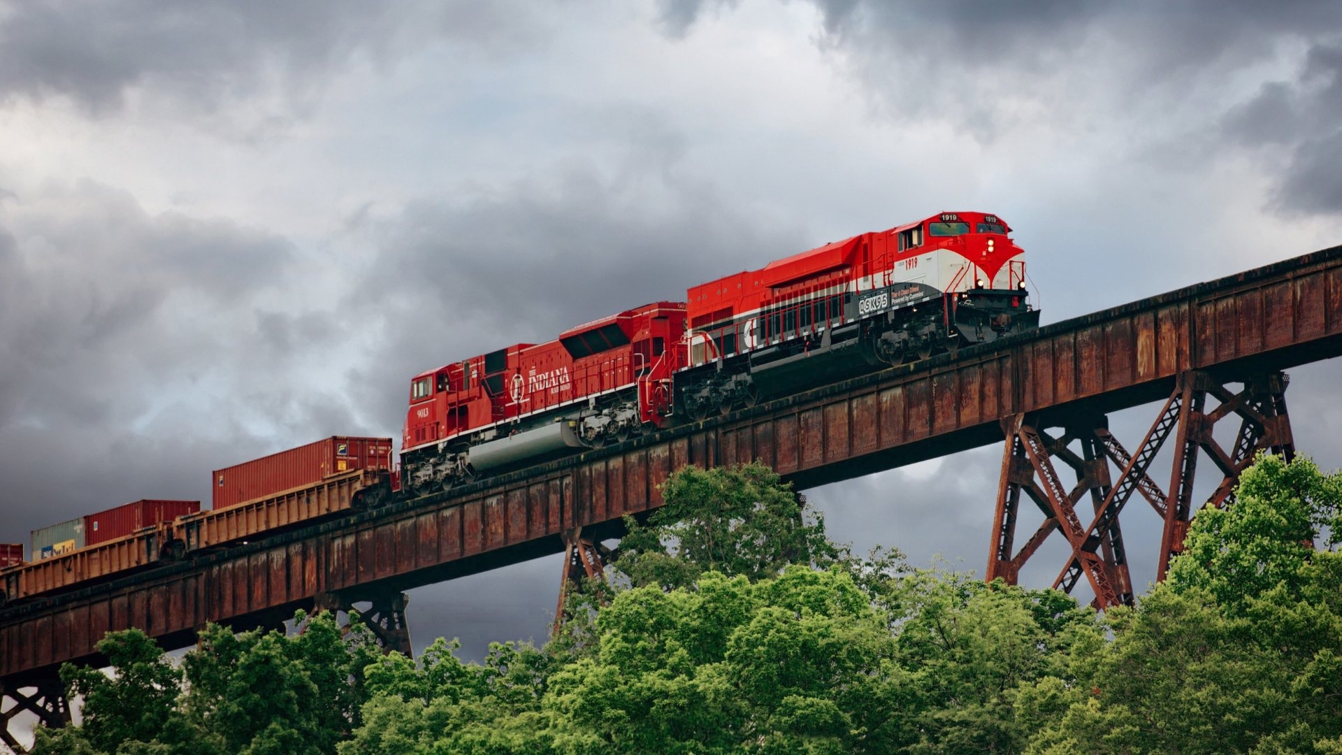 Red freight locomotive pulling intermodal rail cars across a steel trestle bridge, demonstrating modern rail transportation and rail engine performance