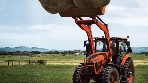 tractor hoisting up bails of hay