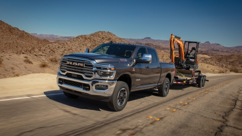 Ram truck hauling a compact excavator on a trailer along an open road