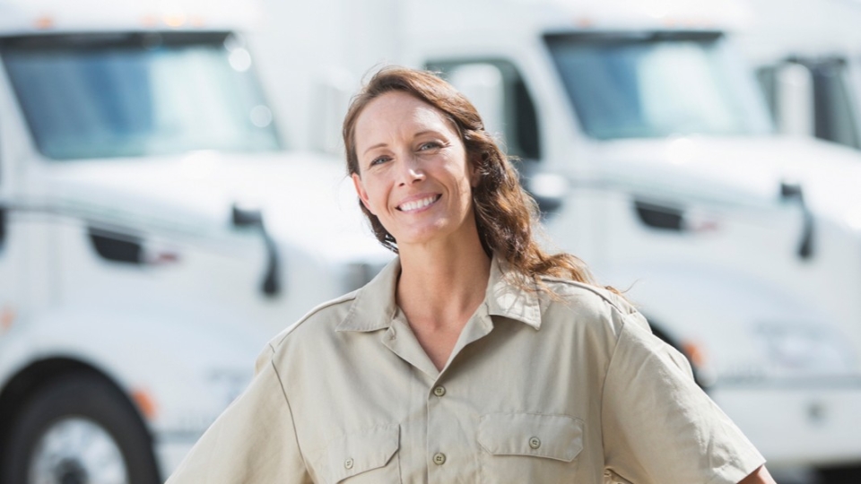A happy remote truck fleet manager smiling with semi trucks blurred in the background
