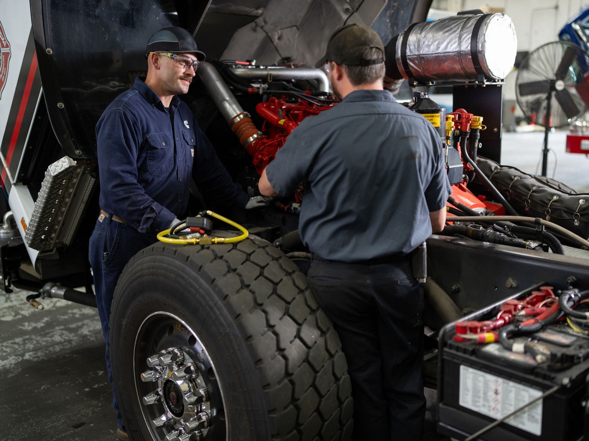 Two technicians performing maintenance on a truck engine in a service shop