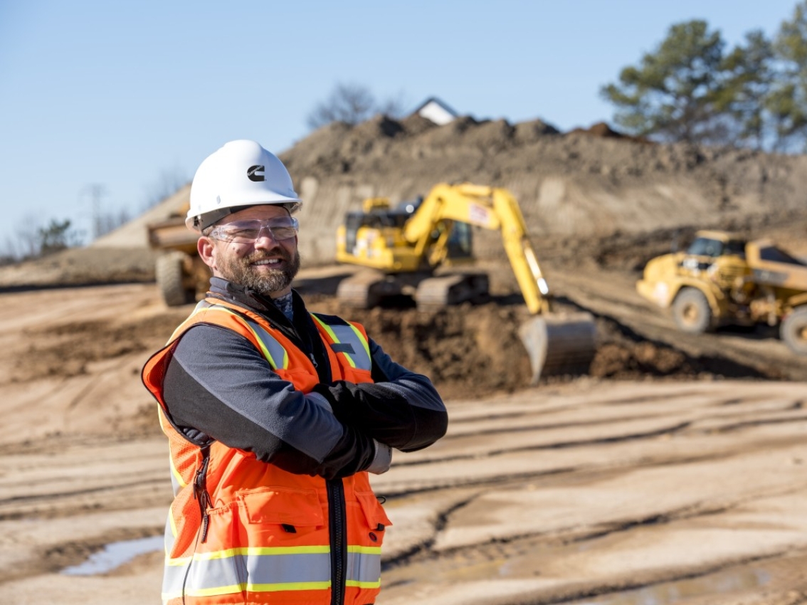 Worker of a mining quarry posing in front of multiple mining vehicles